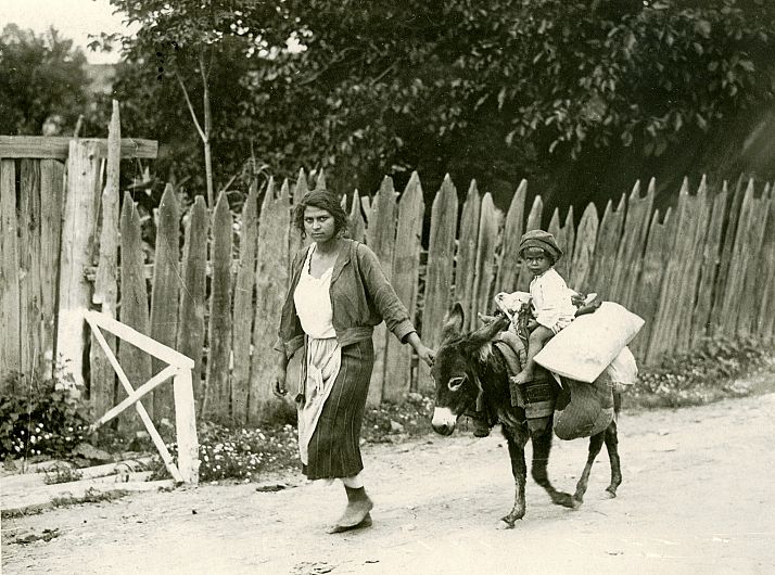 Copil călare pe măgăruș, Nereju, jud. Vrancea (1927) Imaginea surprinsă de obiectivul aparatului de fotografiat aduce în fața privitorului o secvență din lumea satului: o femeie care trage după ea un măgăruș pe care este așezat un copil și alte mărfuri. Sunt pe un drum comunal mărginit de un gard din scânduri de lemn cu capetele crestate.Fotograf: Iosif Berman Instituția de proveniență: Muzeul Național al Satului Dimitrie Gusti - București